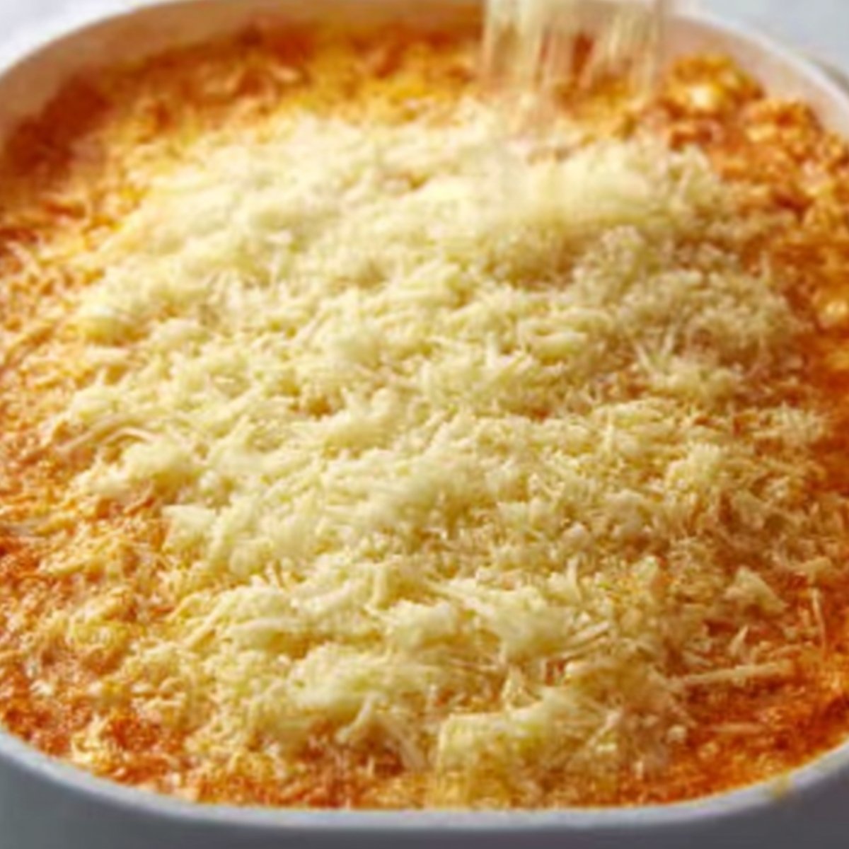 The Best Buffalo Chicken Dip Recipe 10 "Shredded cheese being sprinkled on top of the prepared Buffalo Chicken Dip before baking."