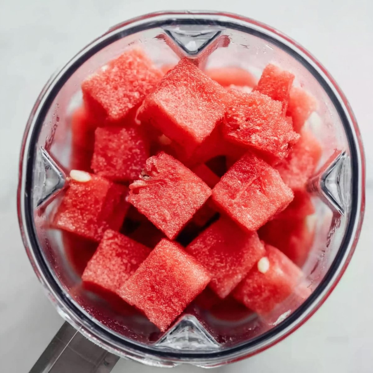 The Best Watermelon Slushie Recipe 11 Top-down view of a blender filled with evenly cut frozen watermelon cubes, bright red with visible ice crystals.