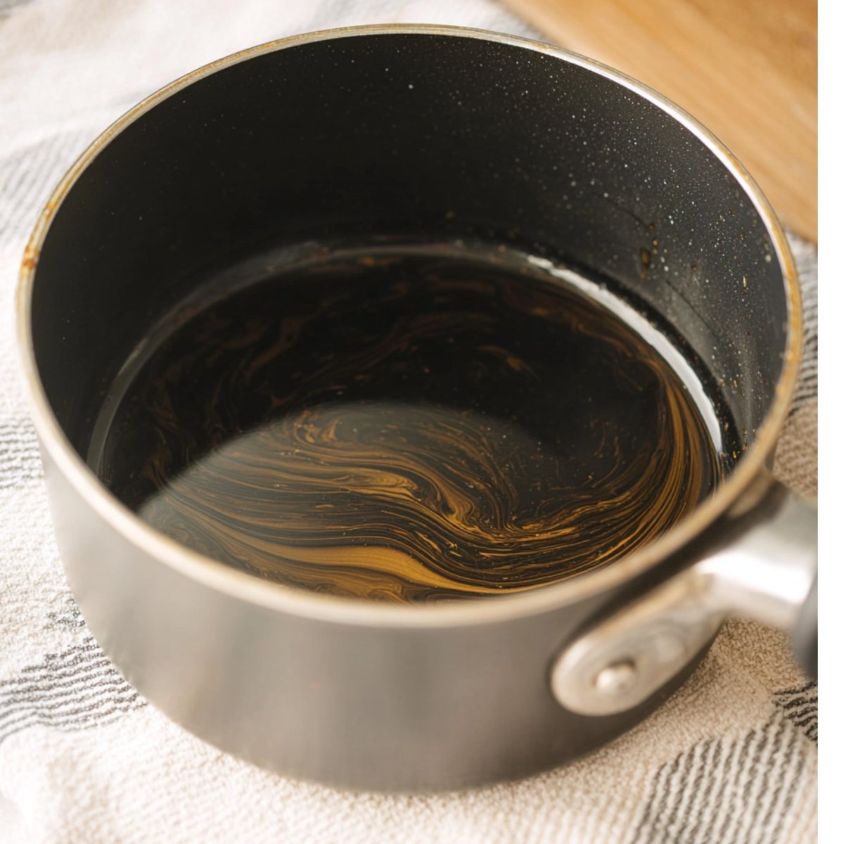The Best Gingerbread White Russian Recipe 10 Close up of a dark, glossy liquid swirling in a saucepan. The rich texture of the liquid suggests it’s likely a syrup or coffee mixture, resting in the pot ready for further preparation.