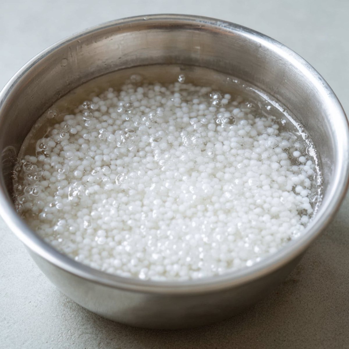 Healthy Mango Tapioca Pudding Recipe 10 A close-up of tapioca pearls cooking in a metal bowl. The pearls are floating in a bubbly liquid, showing their soft and translucent texture.