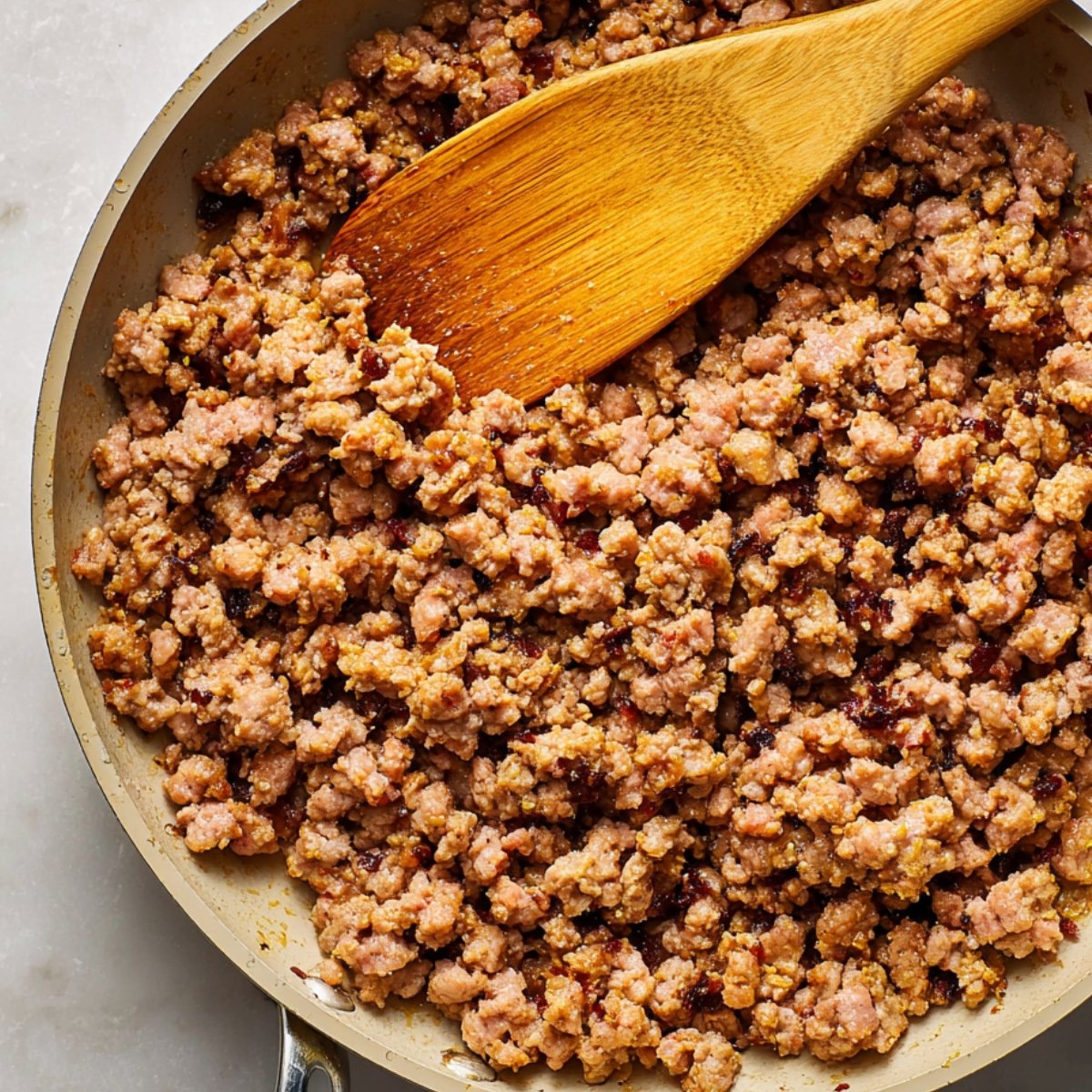 Easy Homemade McGriddle Muffins Recipe 10 A close-up of crumbled sausage cooking in a skillet, with a wooden spoon stirring the meat. The sausage is browned and evenly cooked, ready to be added to the muffin mixture.