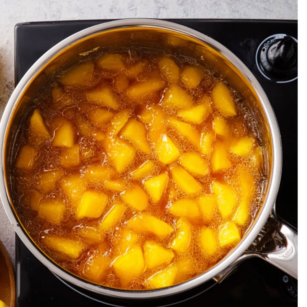 Delicious Peach Lemonade Recipe 11 A pot with chopped peaches simmering in a golden syrupy liquid on a stovetop, with bubbles rising as it cooks.