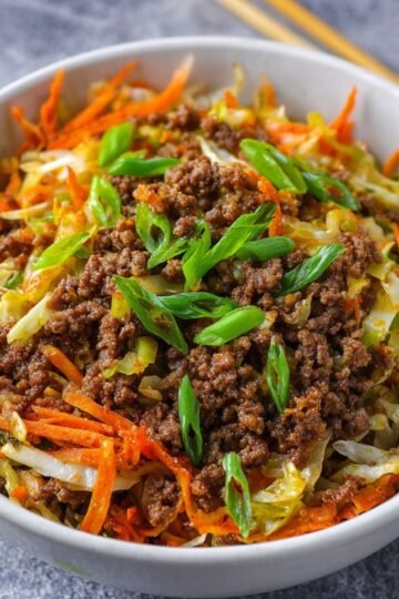 Delicious Egg Roll in a Bowl Recipe 12 Egg Roll in a Bowl of cooked ground beef mixed with shredded cabbage and carrots, garnished with sliced green onions.