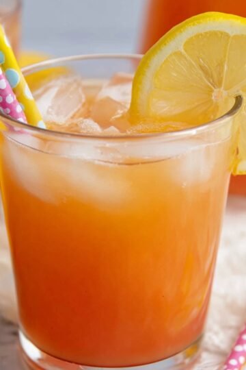 Easy Guava White Tea Lemonade Recipe 16 Close up of a refreshing glass of iced guava white tea lemonade, garnished with a lemon slice and two colorful straws, with ice cubes filling the glass.