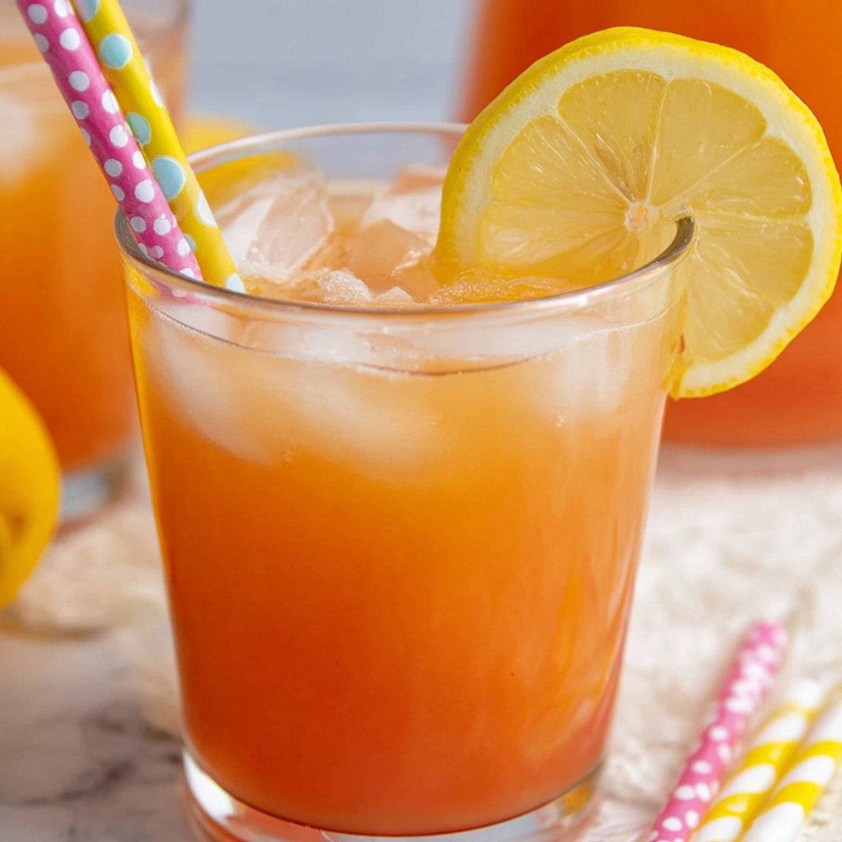 Easy Guava White Tea Lemonade Recipe 9 Close up of a refreshing glass of iced guava white tea lemonade, garnished with a lemon slice and two colorful straws, with ice cubes filling the glass.