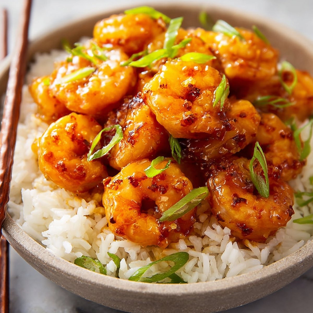 Honey garlic shrimp served on a bed of white rice, garnished with chopped green onions.
