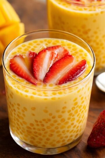 Healthy Mango Tapioca Pudding Recipe 14 A delicious serving of mango tapioca pudding in a glass cup, topped with fresh strawberry slices. The pudding features smooth, golden-yellow tapioca pearls, creating a tropical dessert.