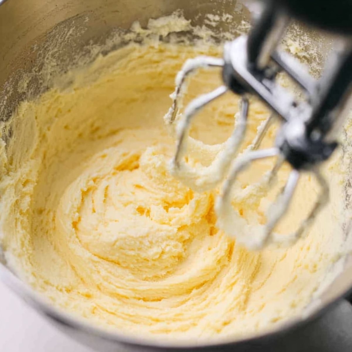 The Best lemon Blueberry Bread Recipe 10 Close up of a stand mixer with beaters mixing a creamy butter and sugar mixture in a silver mixing bowl.