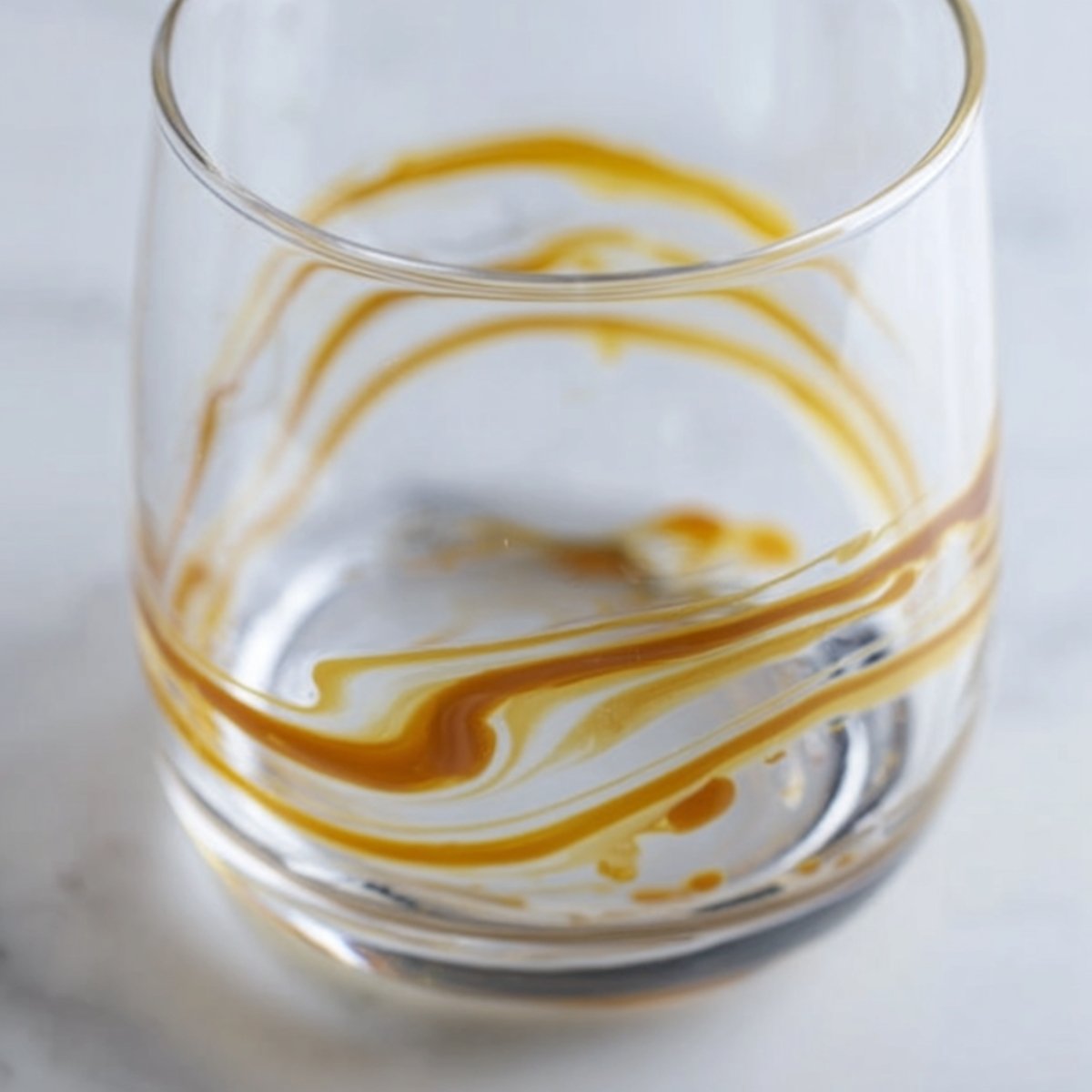 Easy Salted Caramel White Russian Cocktail 10 Close up of an empty glass with caramel syrup swirled on the inside, ready for a drink to be poured. The syrup leaves a golden swirl pattern, adding a decorative touch to the glass.