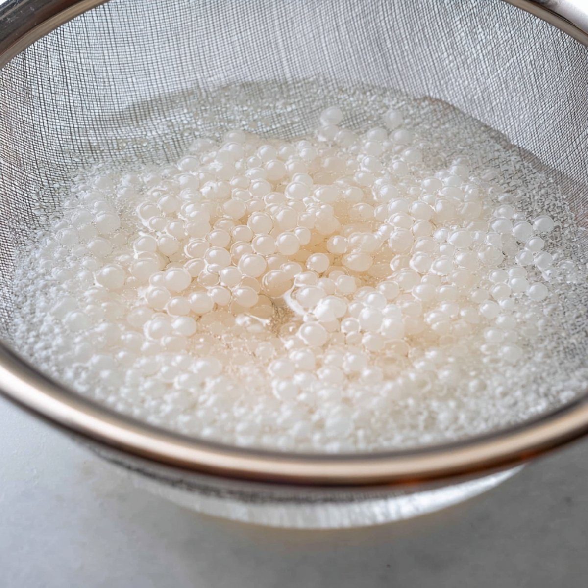 Healthy Mango Tapioca Pudding Recipe 11 Close up of soaked tapioca pearls resting in a fine mesh strainer, with water still surrounding the translucent pearls. The pearls are plump and ready for cooking.