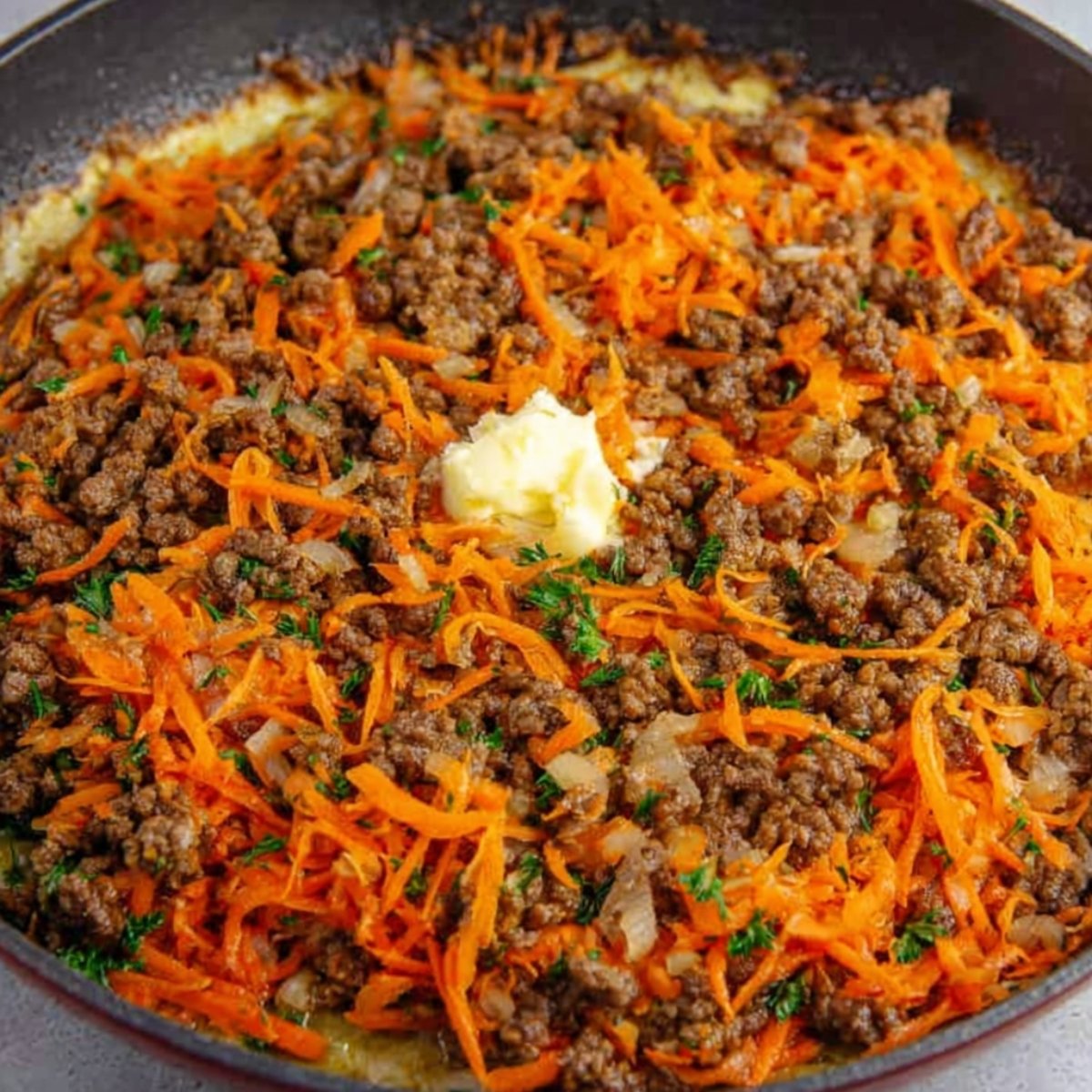Delicious Egg Roll in a Bowl Recipe 10 A skillet with ground beef, shredded carrots, onions, and herbs, with a dollop of butter in the center.