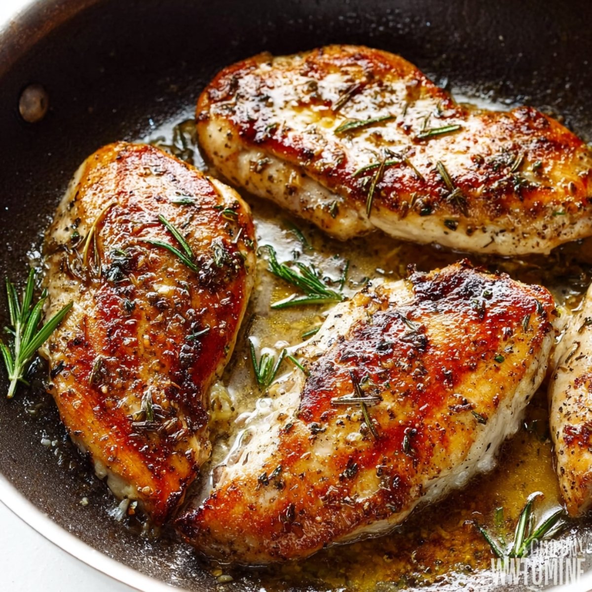 Healthy Garlic Butter Chicken Recipe 11 A close-up of golden-brown, seared chicken breasts in a skillet with fresh rosemary sprigs and a rich buttery sauce.