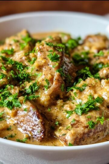 Easy Smothered Chicken And Rice Recipe 3 A bowl of creamy Smothered Chicken and Rice, garnished with fresh green parsley. The chicken pieces are coated in a rich gravy with a smooth texture, resting on top of the rice.