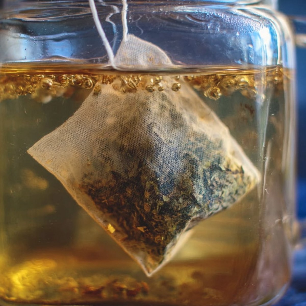 Easy Guava White Tea Lemonade Recipe 11 Close up of a tea bag submerged in warm water, with loose-leaf herbs inside the bag slowly releasing their color, creating a golden tea infusion.