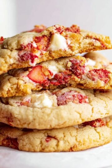 Healthy Strawberry Cheesecake Cookies 16 A stack of freshly baked strawberry cheesecake cookies with a bite taken out of one, showing the gooey interior with strawberry pieces.