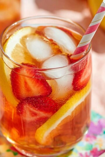 The Best Strawberry Iced Tea Recipe 1 A refreshing glass of strawberry iced tea garnished with slices of lemon and strawberries, served with ice and a striped straw.