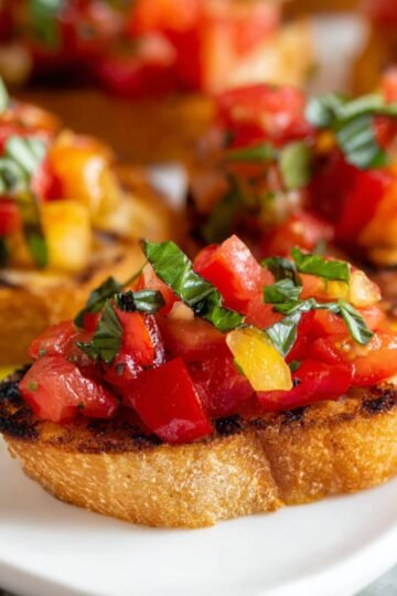The Best Tomato Bruschetta Recipe 22 A plate of Tomato Bruschetta with grilled bread slices topped with a mixture of diced tomatoes, herbs, and a drizzle of olive oil.