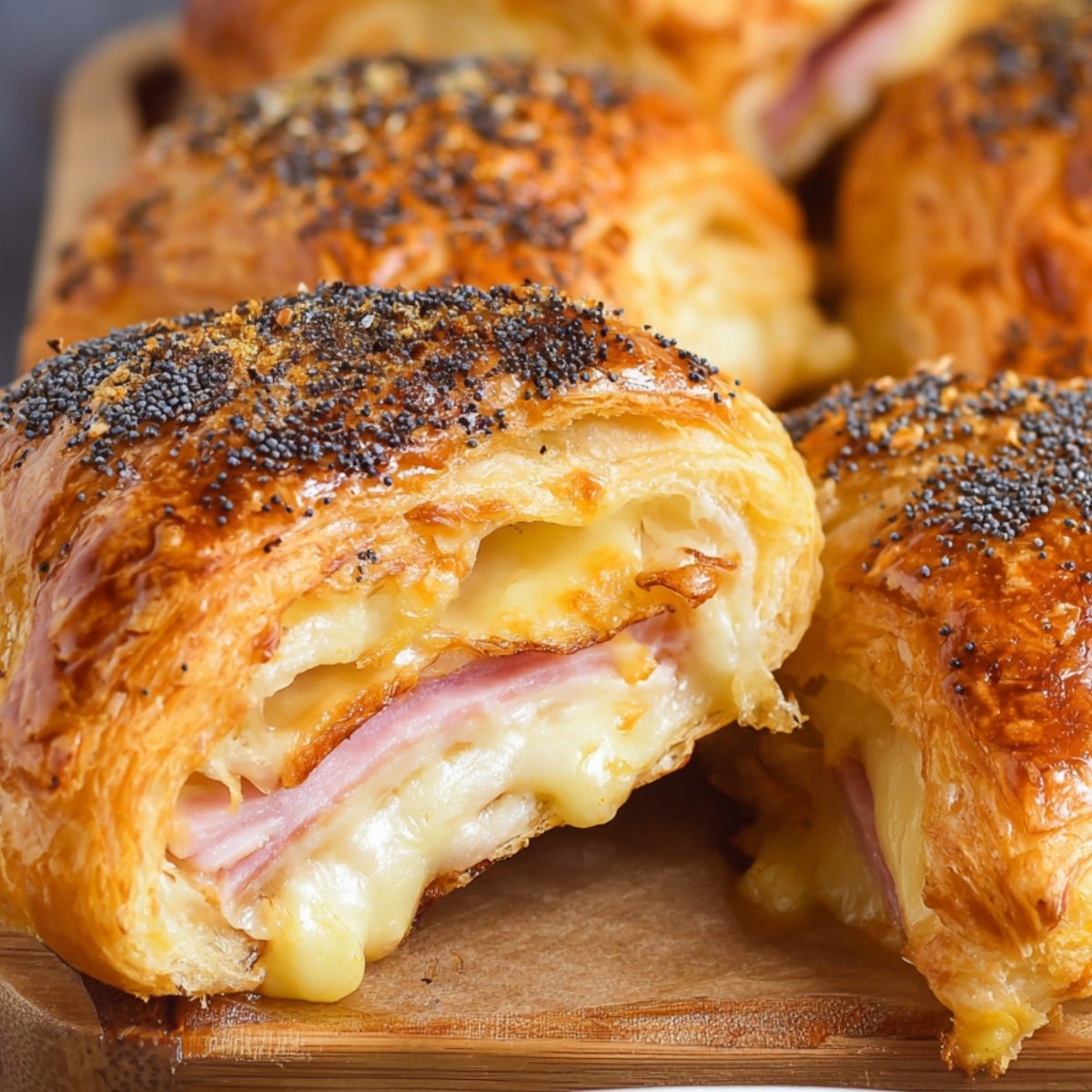 A golden, flaky baked ham and cheese croissants with melted cheese and ham inside, topped with poppy seeds for added flavor.