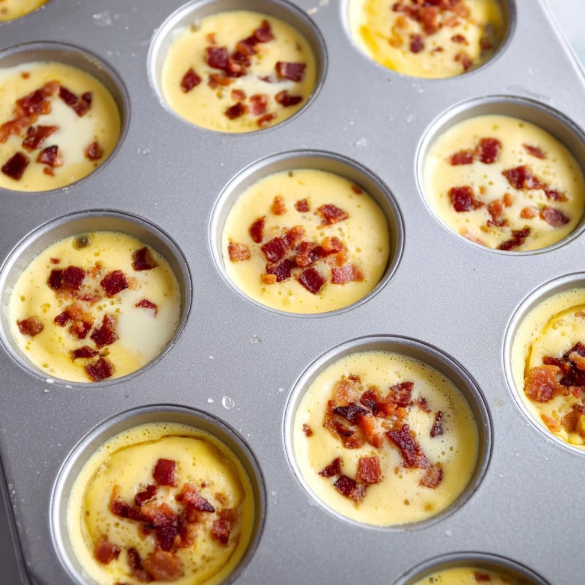 Easy Better Than Starbucks Egg Bites 10 Egg mixture with bacon pieces poured into muffin tin cups before baking