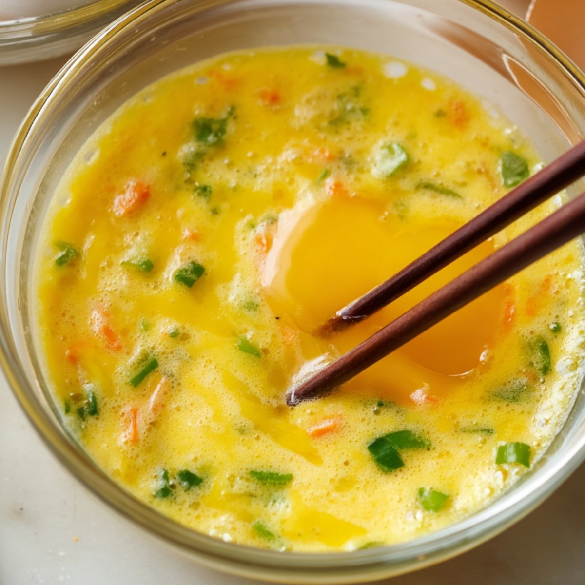 Easy Korean Rolled Omelette 11 A bowl of whisked eggs with chopped vegetables and a raw egg yolk.
