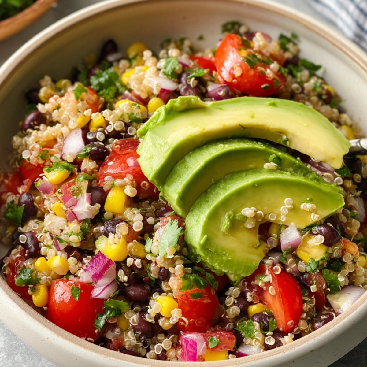 This image shows a Black Bean Quinoa Salad, corn, cherry tomatoes, red onion, cilantro, and avocado slices on top.