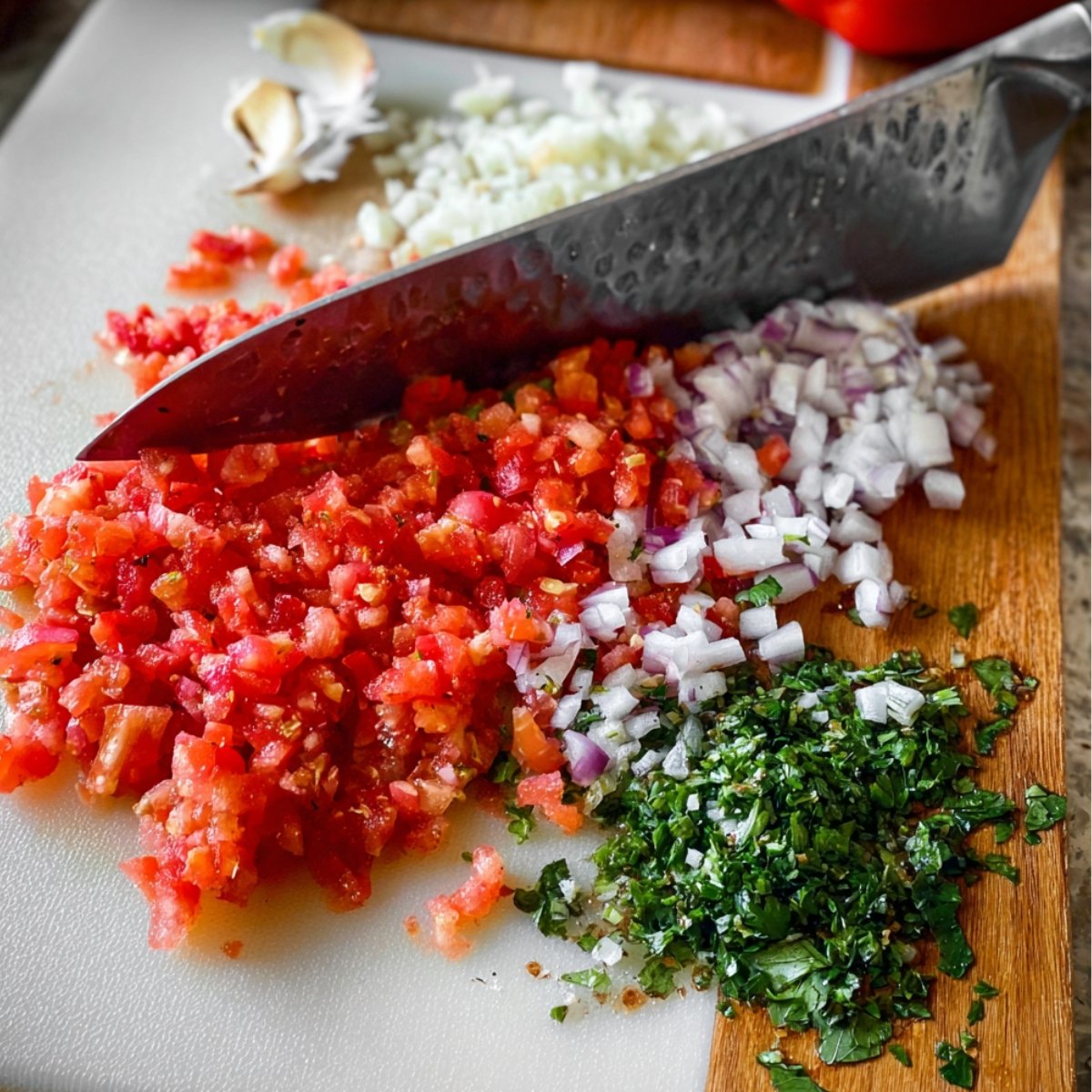 Easy Turkish Ezme Recipe 11 Chopped tomatoes, onions, and cilantro on a cutting board with a knife.