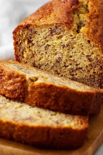 Freshly baked banana bread with slices cut and laid on a wooden board.