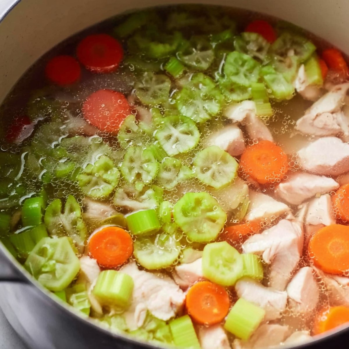 Best Double Crust Chicken Pot Pie 10 Chicken, carrots, celery, and okra simmering in a pot with broth.