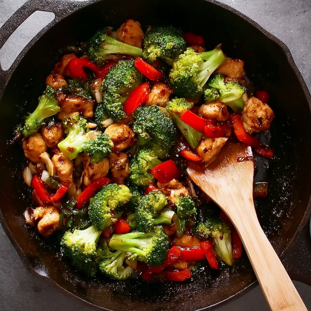 Easy Chicken and Broccoli Noodle Stir Fry Recipe 11 Stir-frying chicken, broccoli, and red peppers in a skillet with a wooden spoon.