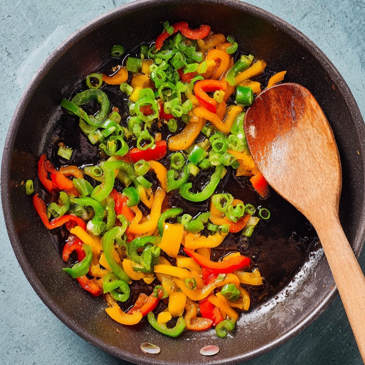 Easy Crispy Salmon Rice Bowls 11 Sautéed bell peppers and green onions in a pan with a wooden spoon.