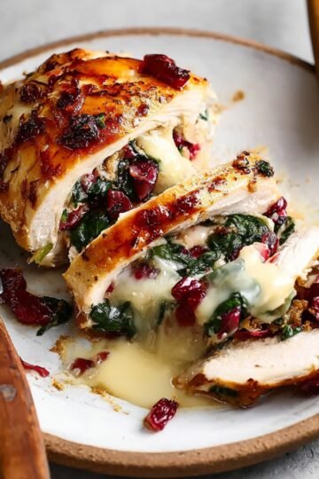 Easy Cranberry Brie Stuffed Chicken Breasts 7 A sliced Cranberry Brie Stuffed Chicken Breasts, with cheese and spinach spilling out.