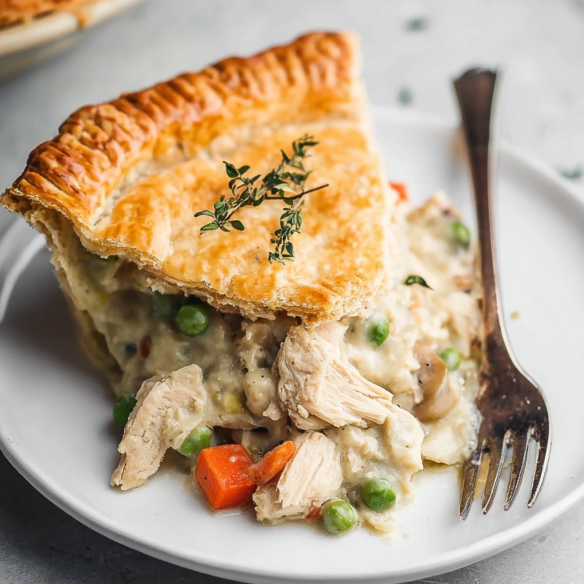 Slice of Crust Chicken Pot Pie with vegetables and a golden, flaky crust, garnished with thyme.