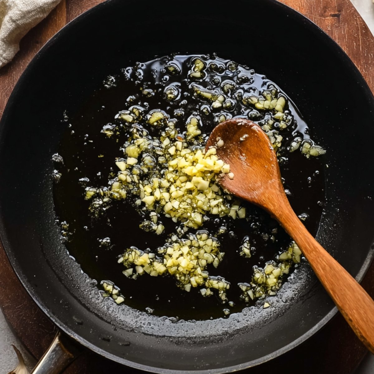 Easy Sweet Potato Curry with Chickpeas and Spinach 10 Chopped garlic sautéing in olive oil in a black skillet, with a wooden spoon stirring.