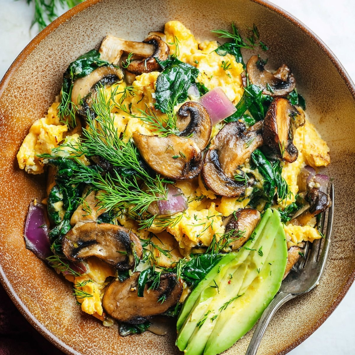A delicious Spinach mushroom egg scramble, garnished with fresh dill and avocado slices.
