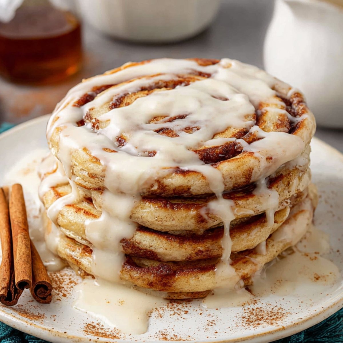 Stack of cinnamon roll pancakes drizzled with cream cheese icing and served with cinnamon sticks.