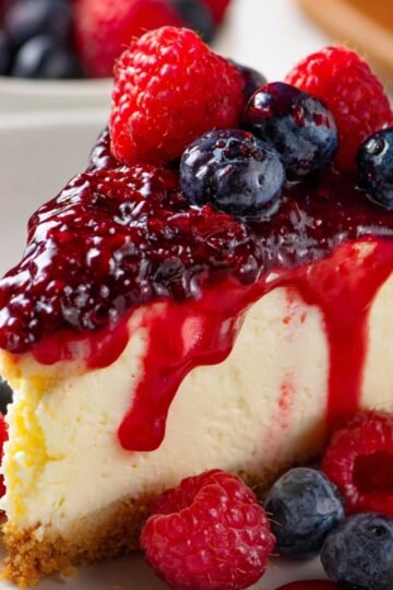 Easy Keto Cheesecake Recipe 4 A slice of keto cheesecake topped with raspberry and blueberry sauce.