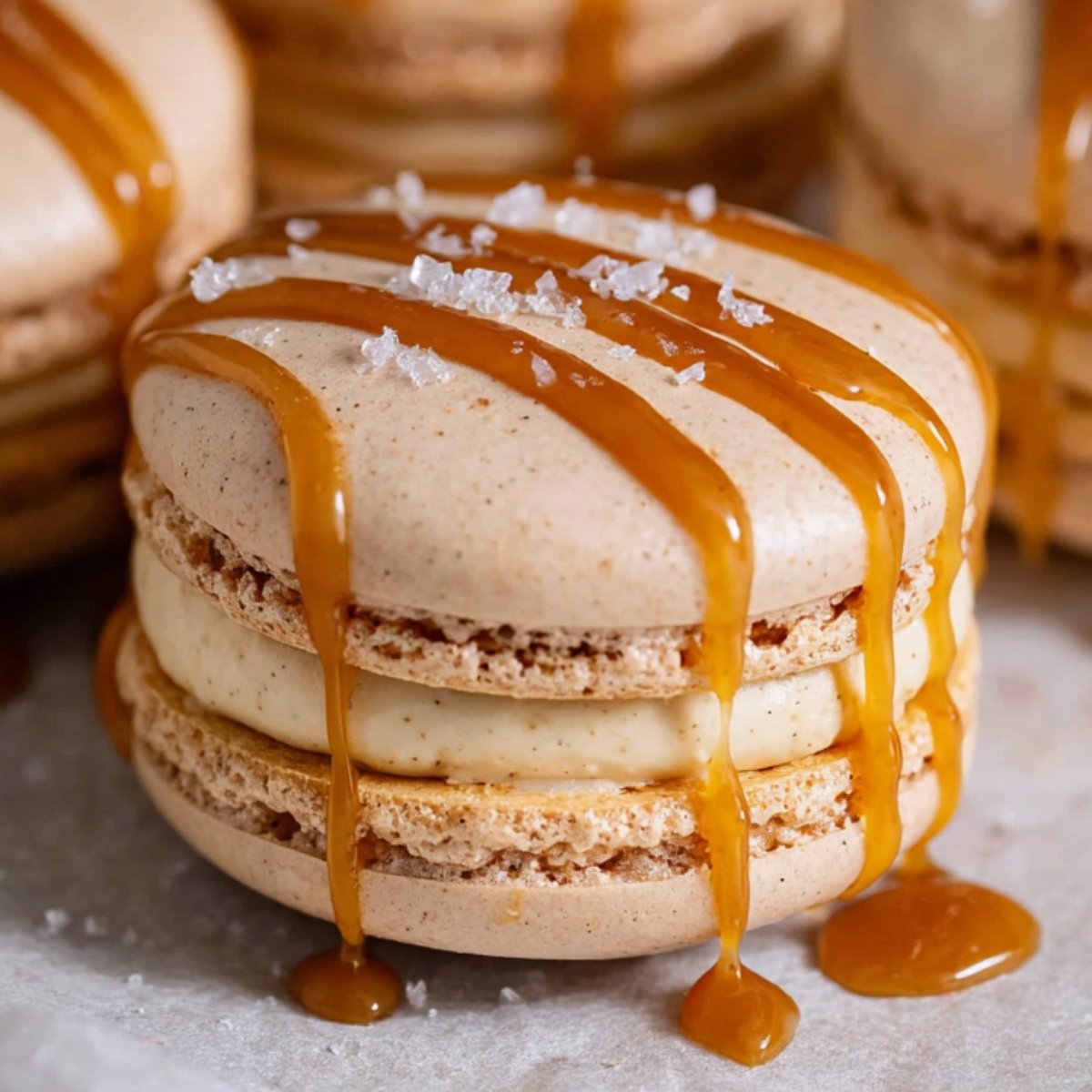 Close-up of a salted caramel macarons filled with creamy frosting and topped with flaky sea salt.