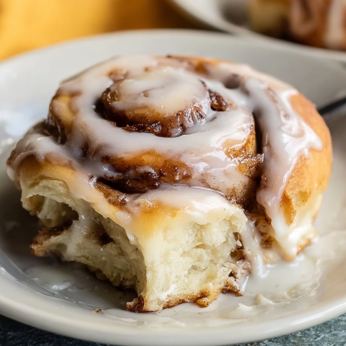 The image shows a soft cinnamon rolls with icing, partially cut to reveal its fluffy interior.