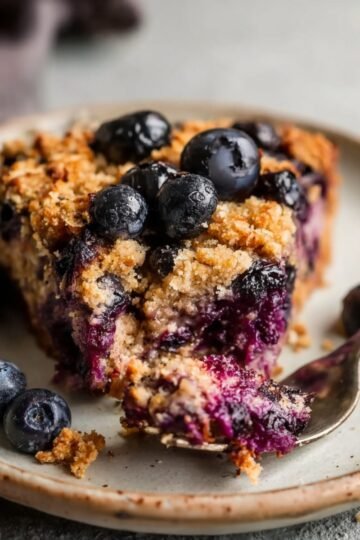 Easy Blueberry Baked Oatmeal 16 A slice of Blueberry Baked Oatmeal on a plate with fresh blueberries on top.