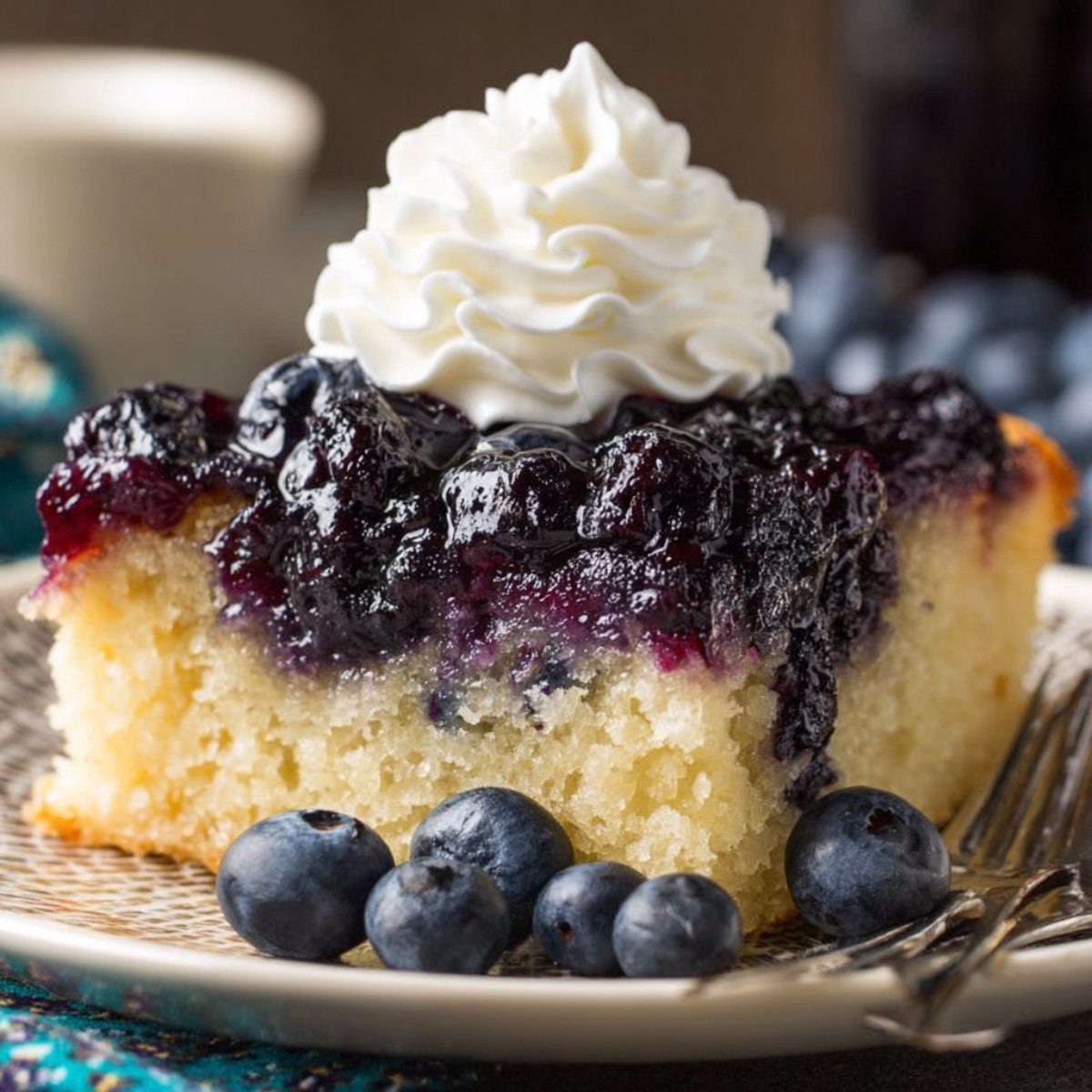 A slice of Blueberry Upside Down Cake topped with whipped cream and fresh blueberries.