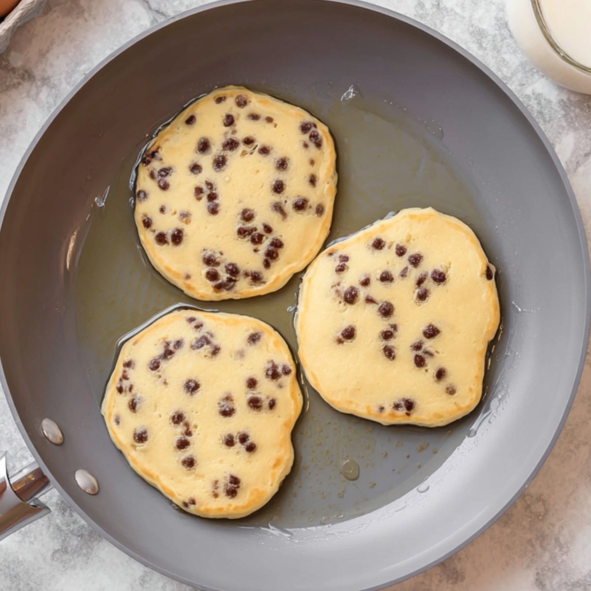 Best Chocolate Chip Pancakes Recipe 11 Chocolate chip pancakes cooking in a pan.
