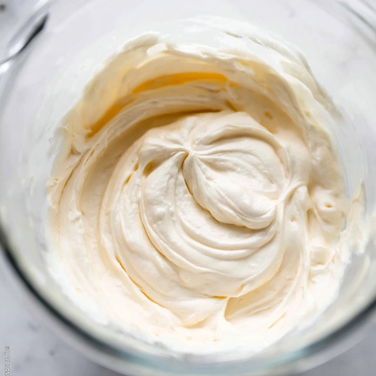 Easy Lemon Blueberry Cupcakes 11 Bowl of creamy frosting swirled with spatula.