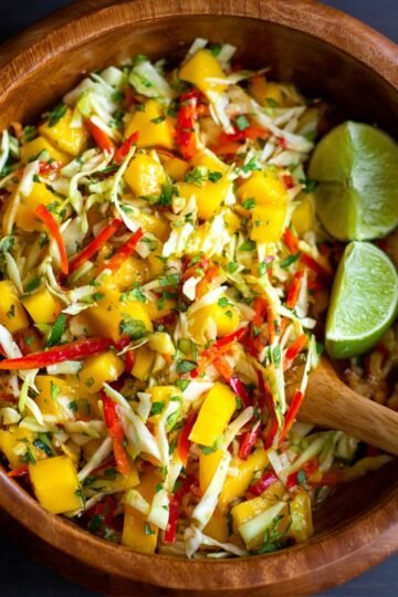 Easy Mango Slaw Recipe 1 Mango Slaw with shredded cabbage, red chili, and lime wedges in a wooden bowl.