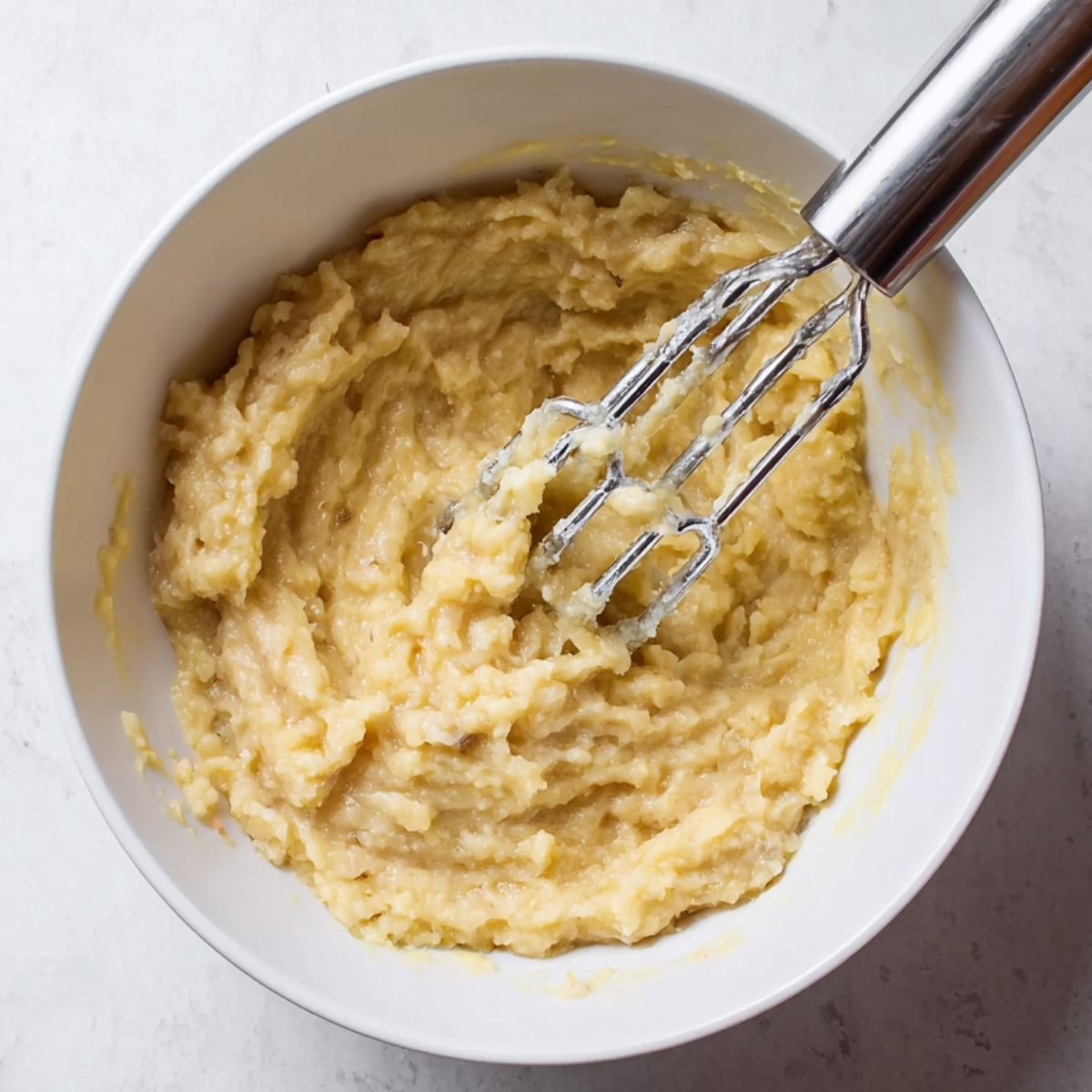 Healthy Banana Muffins Recipe 10 Mashed bananas in a white bowl with a whisk.