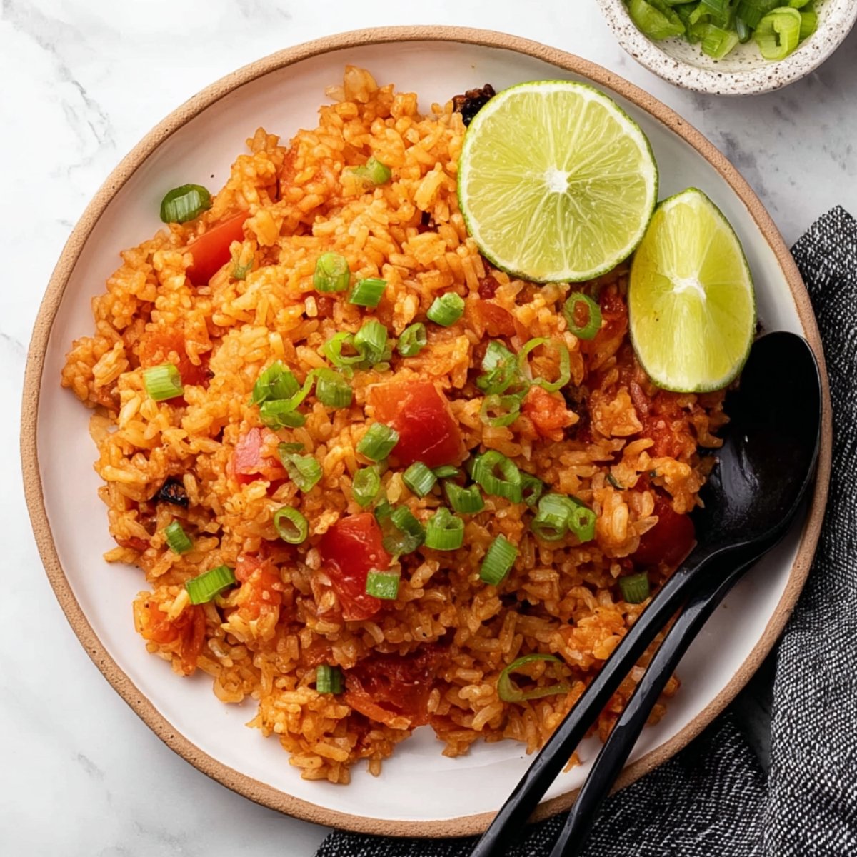 Plate of tomato rice garnished with lime and green onions.
